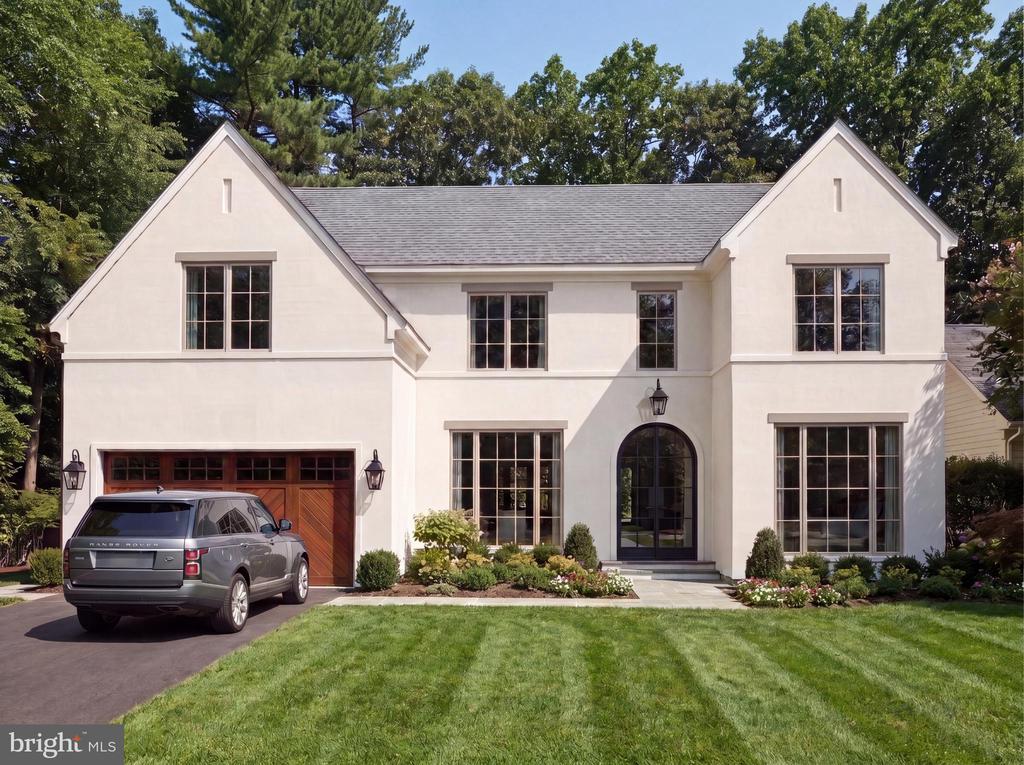 White two-story house with steep gables, an arched entry, wooden garage door, and gray SUV in the driveway.