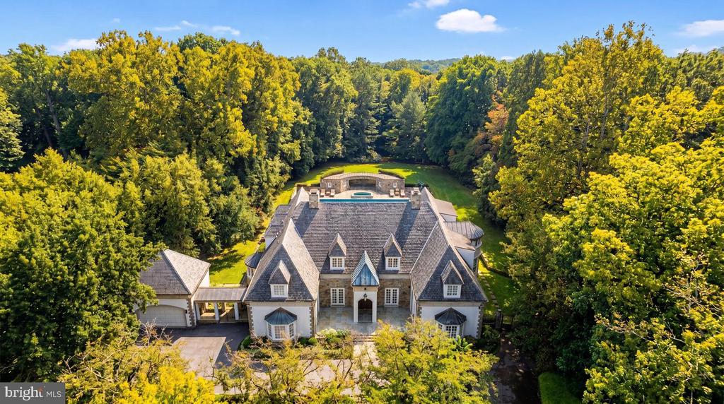 Aerial view of a large gabled home surrounded by autumn trees, with a pool behind it.
