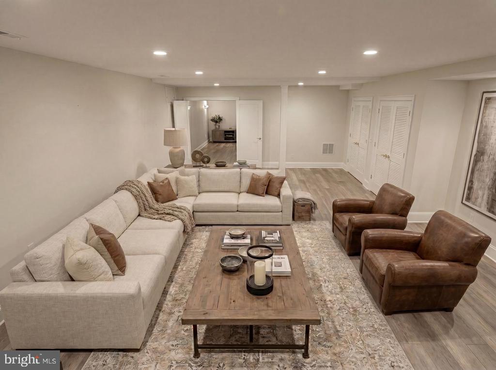 Staged basement living room with a cream sectional, brown leather armchairs, and a large wooden coffee table.
