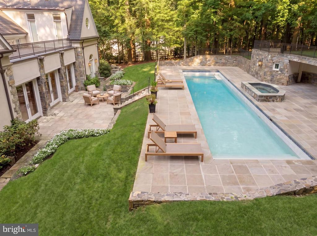 Backyard swimming pool and raised hot tub beside a stone patio, lawn, and mature trees.
