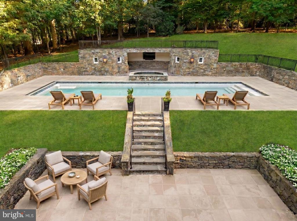 Backyard pool with stone walls, a covered fireplace, and tiered patios with outdoor seating.