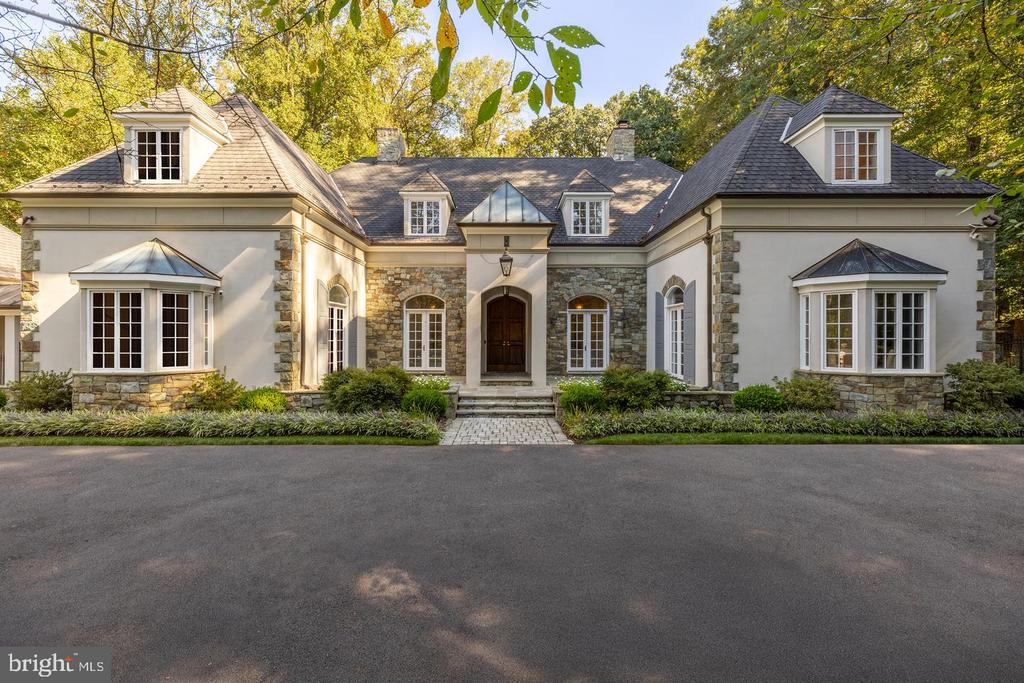 Home with stone accents, a central arched entrance, dormers, and autumn trees.