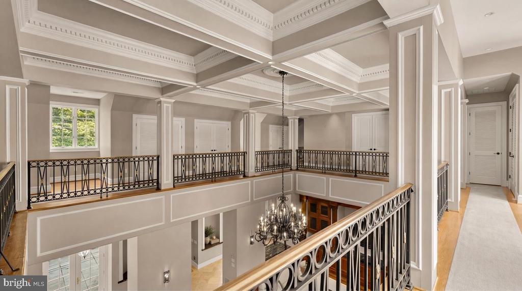 Upper-level landing overlooking a two-story foyer, with ornate iron railings and a coffered ceiling.