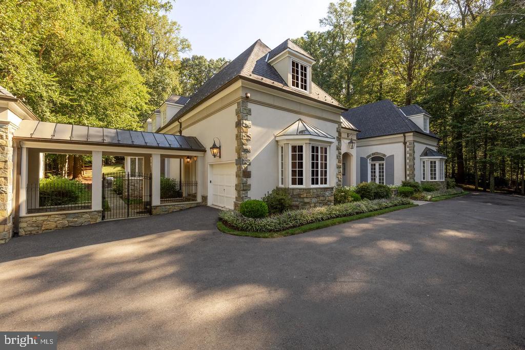 Cream-colored house with stone accents, a covered gated entry, and a wide paved driveway.
