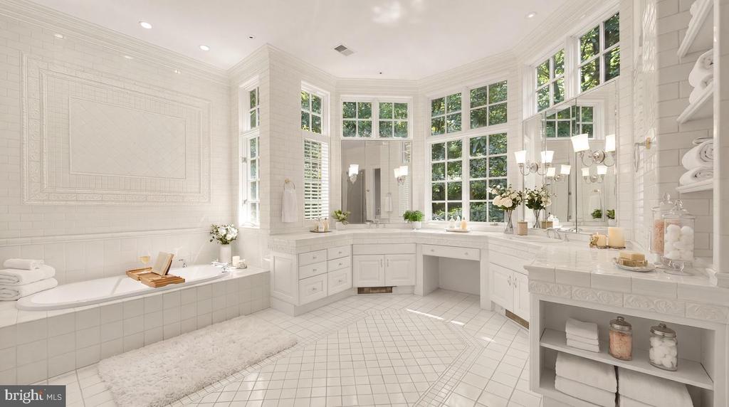 Bright white bathroom with a soaking tub, extensive vanity, and tall windows overlooking greenery.