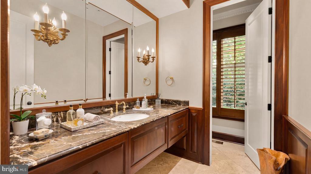 Bathroom vanity with dark marble counters, wood cabinetry, framed mirrors, and a doorway to a shuttered toilet area.