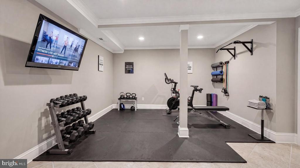 Home gym with dumbbell rack, exercise bike, weight bench, and wall-mounted pull-up bar.