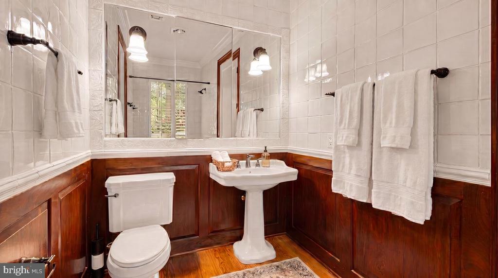 Bathroom with a pedestal sink, dark wood wainscoting, and white tiled walls.