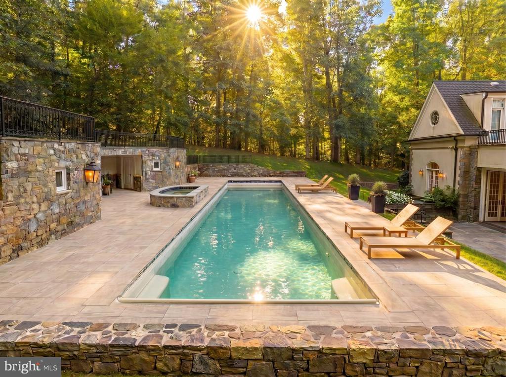 Outdoor pool and spa beside the home, surrounded by stone paving and autumn trees.