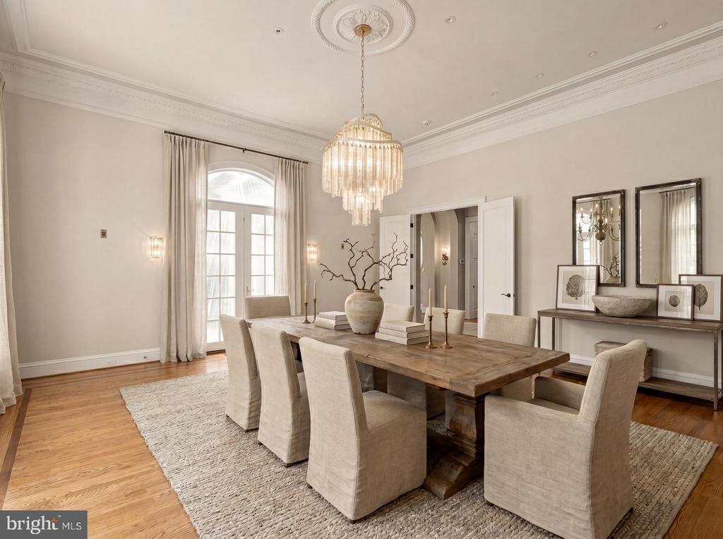 Dining room with a rustic wood table, upholstered chairs, French doors, and a crystal chandelier.