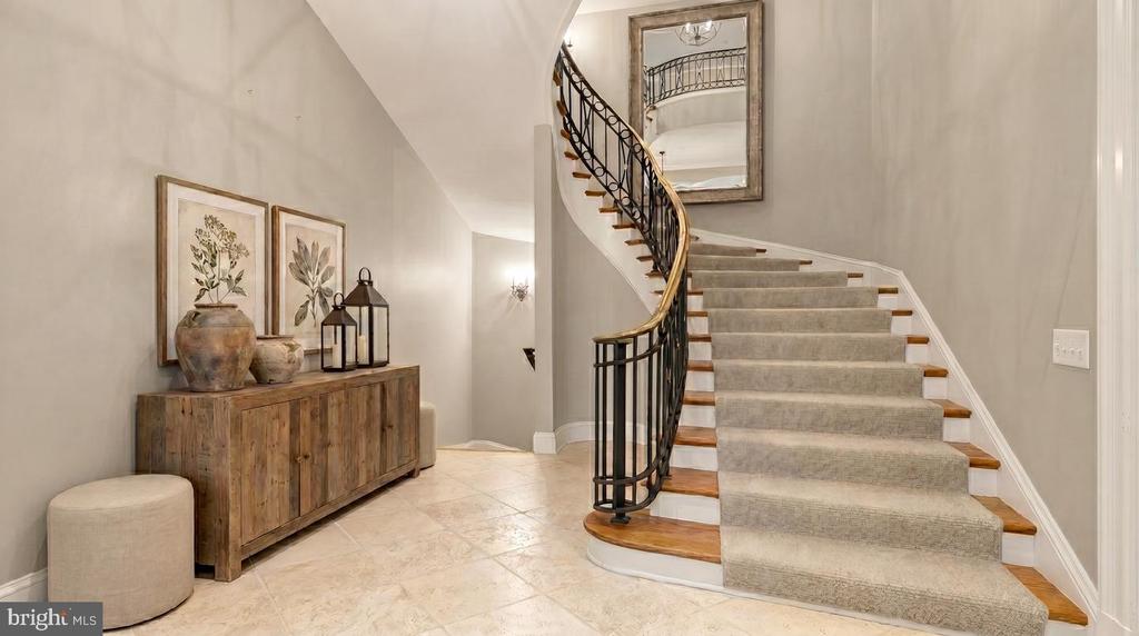 Foyer with a sweeping carpeted staircase, curved iron railing, and rustic console cabinet.