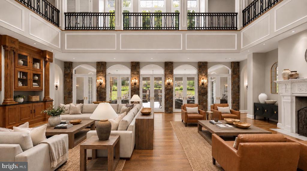 Two-story living room with a balcony railing, stone columns, and tall windows opening to a landscaped yard.