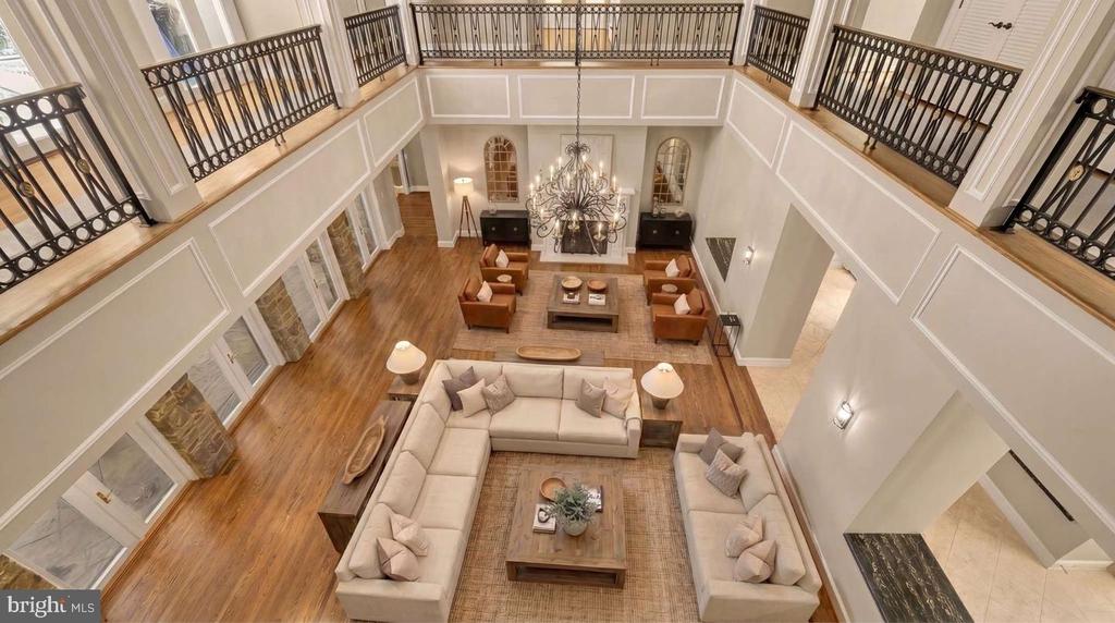 Double-height living room with cream sectional seating, hardwood floors, chandelier, and black-railed balcony.