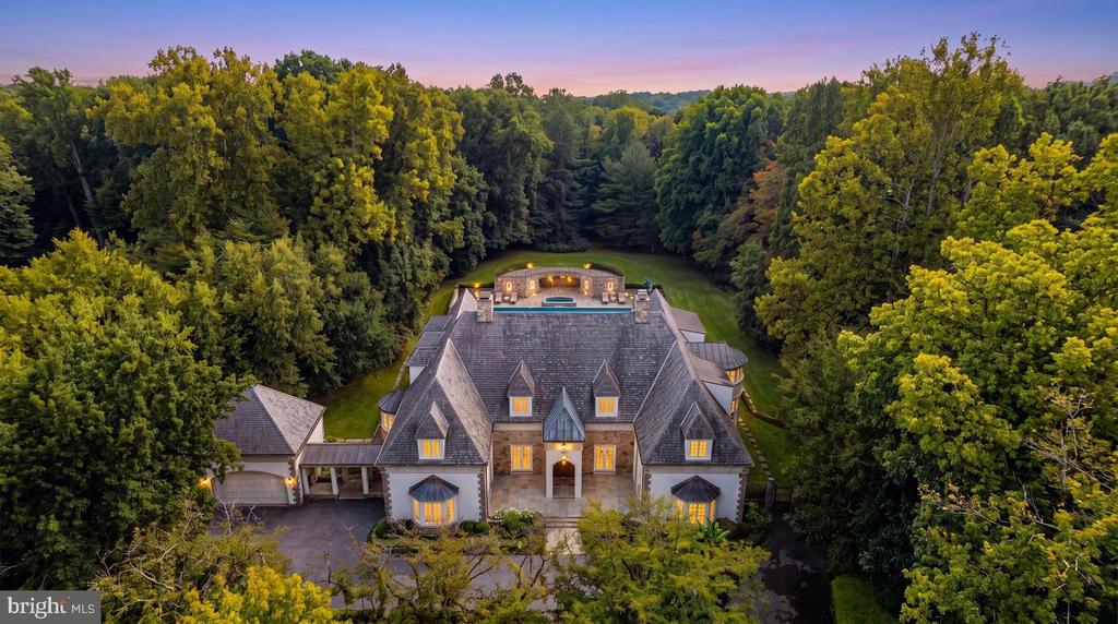 Aerial view of a large gabled estate surrounded by dense trees at dusk.