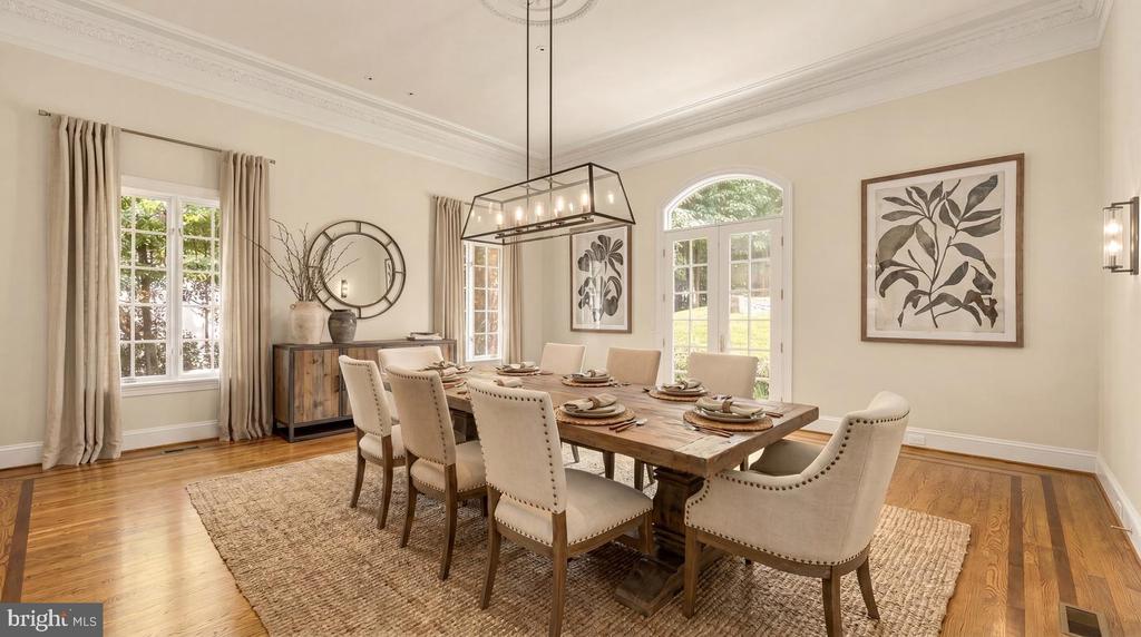 Staged dining room with a long wooden table, upholstered chairs, hardwood floors, and an arched window.