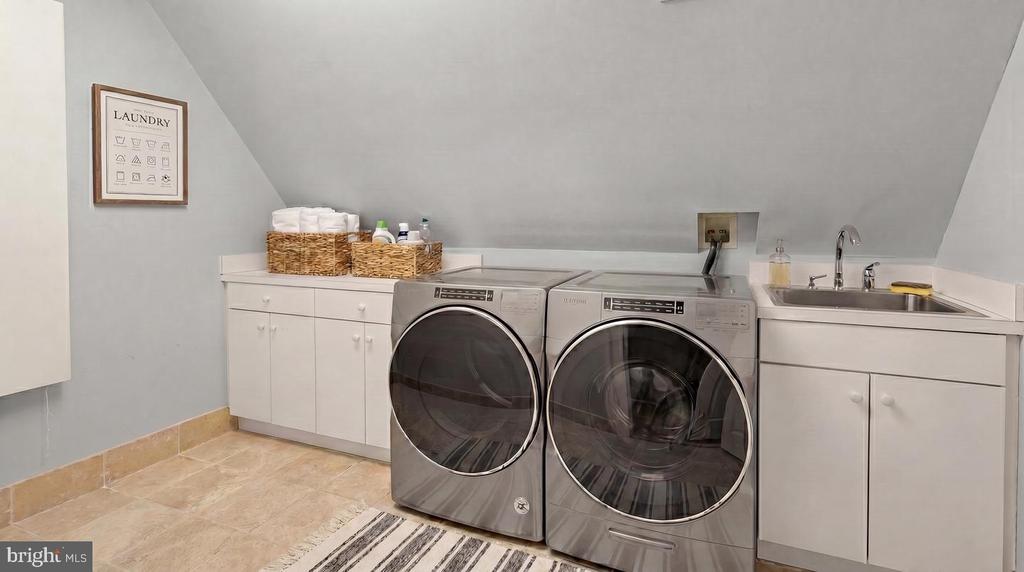 Laundry room with front-loading washer and dryer, white cabinetry, and a utility sink.