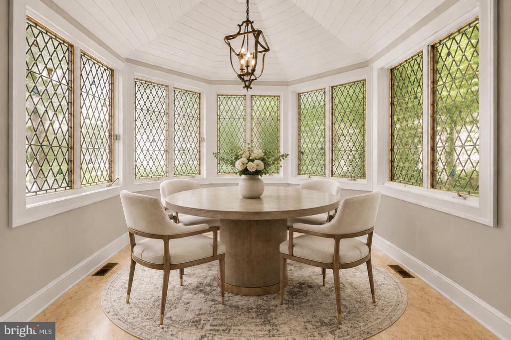 Dining room with a round table, chandelier, and tall diamond-leaded windows.
