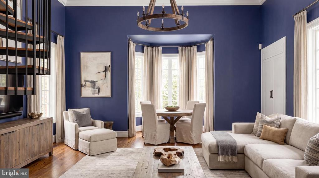 Living room with deep blue walls, white sectional sofa, built-in shelving, and a bright bay-window dining area.