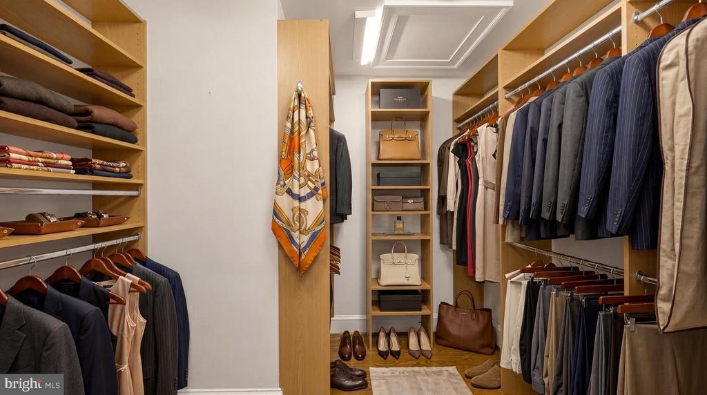 Walk-in closet with wood shelving, hanging clothes, handbags, and shoes.