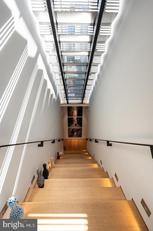 Wood staircase beneath a long slatted skylight, with artwork and sculptural accents along the steps.