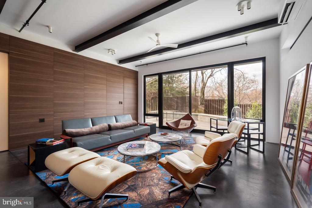 Modern living room with wood-paneled walls, exposed beams, sculptural chairs, and glass doors to a terrace.