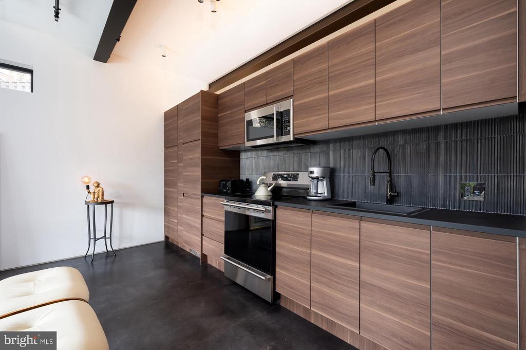 Modern kitchen with warm wood cabinetry, dark tile backsplash, and stainless steel appliances.