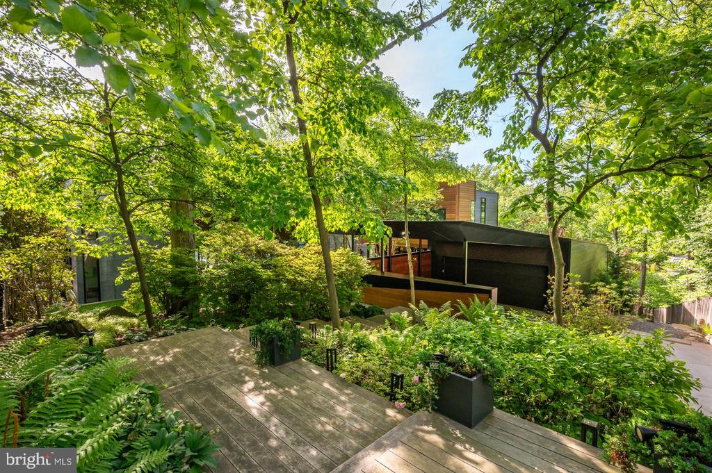Modern dark-clad home nestled among leafy trees, with a broad wooden deck and lush garden.