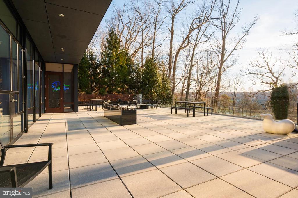 Paved terrace beside a modern home with outdoor seating and views of leafless trees.