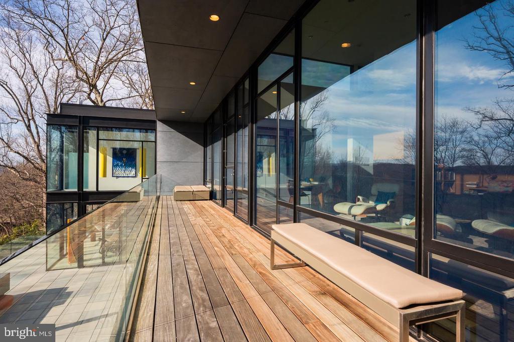 Modern home terrace with glass railings, a wood-plank deck, and a cushioned bench.