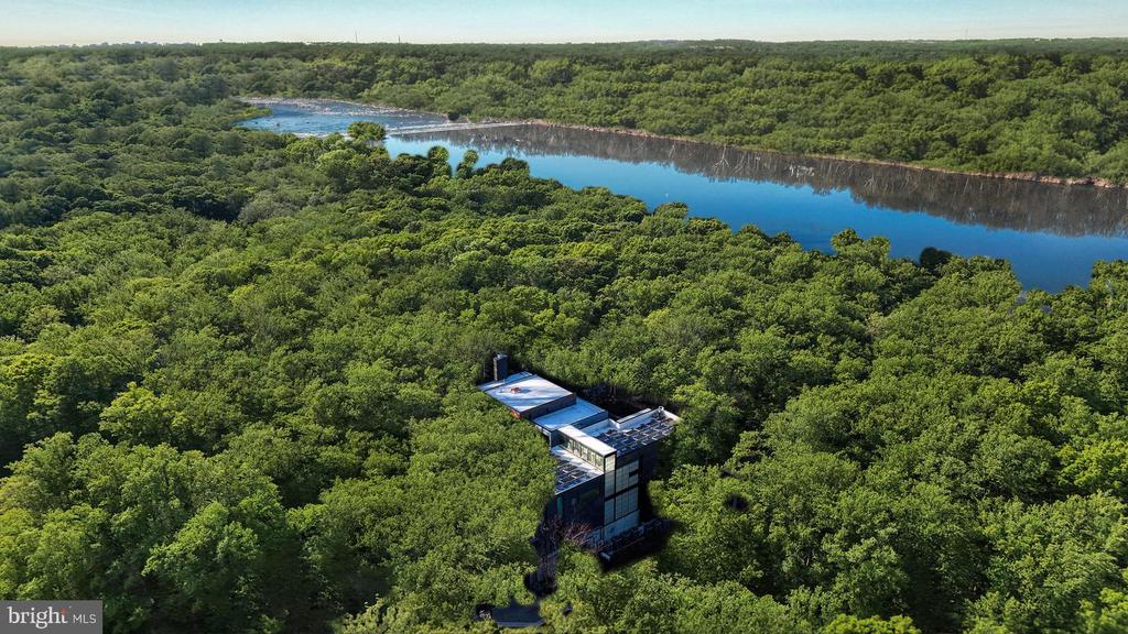 Aerial view of a modern home nestled in dense woods beside a broad river.
