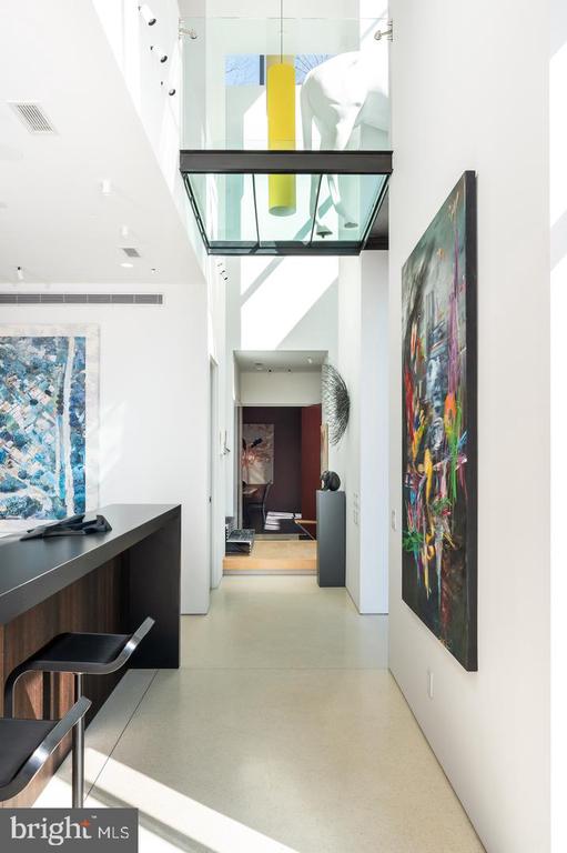 Modern hallway with colorful abstract art, a built-in desk, and a glass overhead bridge.