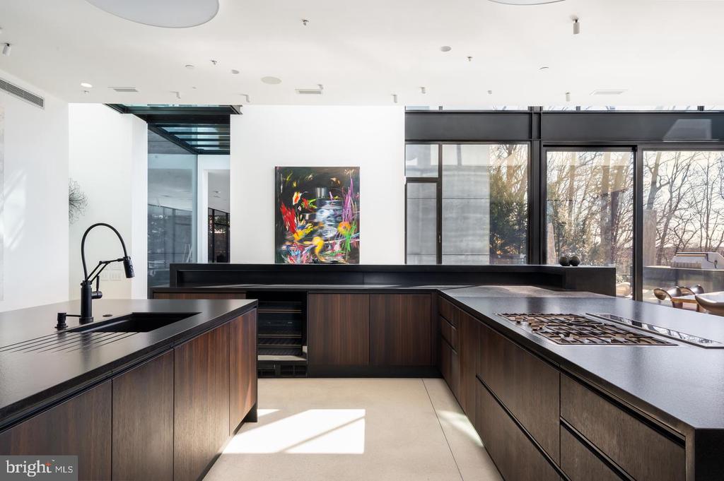 Modern kitchen with dark wood cabinets, a large island cooktop, and floor-to-ceiling windows.