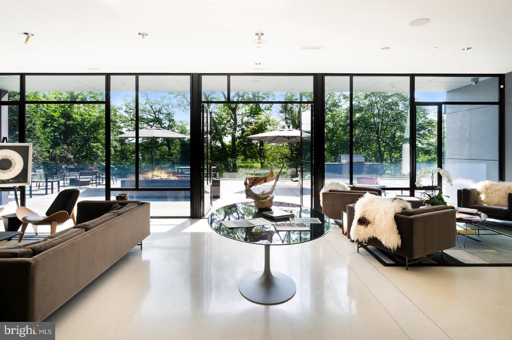 Contemporary living room with floor-to-ceiling glass doors overlooking a pool and leafy trees.