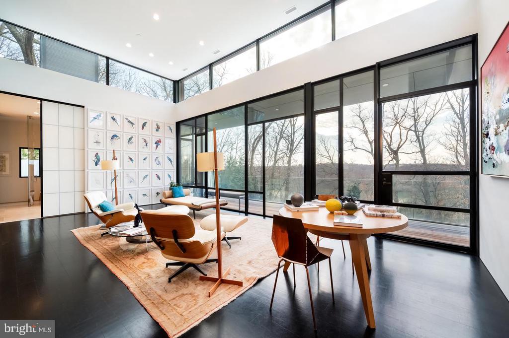 Contemporary living room with lounge chairs and a round dining table beside floor-to-ceiling windows.