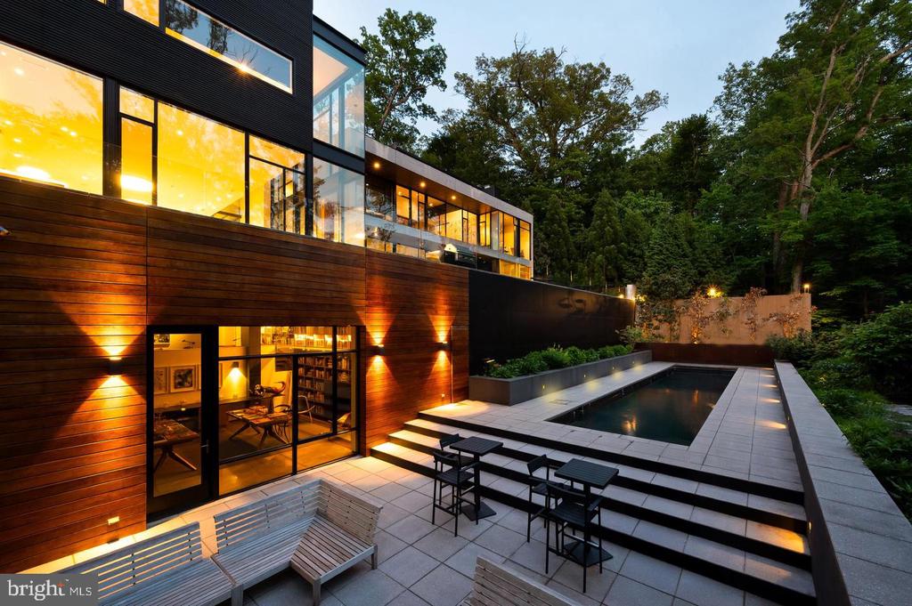 Modern wood-and-glass home with an illuminated swimming pool and patio at dusk.