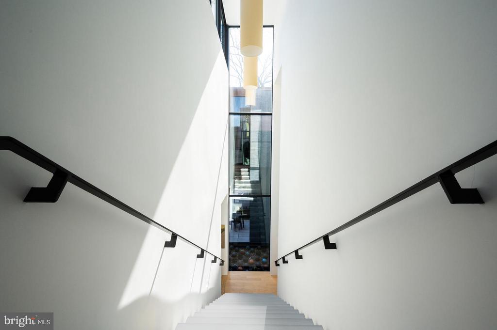 Modern white staircase with black handrails descending toward a tall glass window.