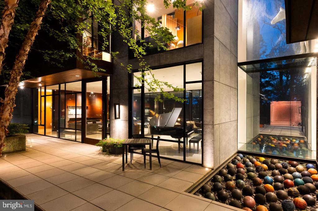 Modern glass-fronted home at night, with a warmly lit patio and a courtyard basin filled with decorative spheres.