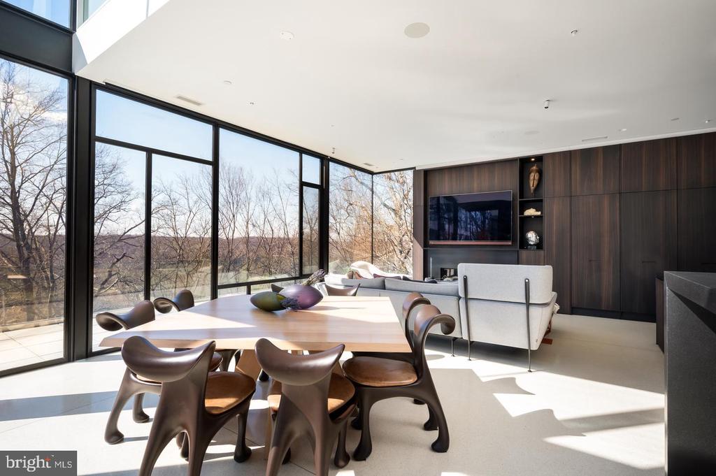 Dining and living area with sculptural chairs, dark wood cabinetry, and floor-to-ceiling windows overlooking trees.