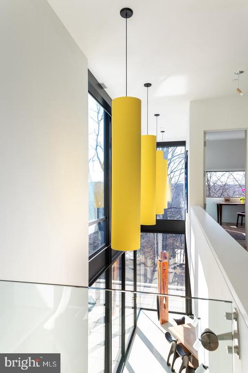 Modern foyer with tall windows, glass railing, and yellow cylindrical pendant lights.