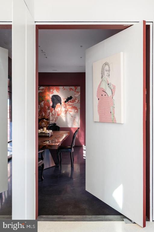 Dining room seen through an open white door, with burgundy walls and colorful artwork.