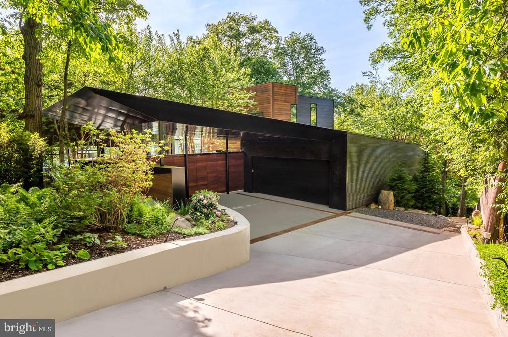 Modern home with dark cladding, wood accents, and a landscaped driveway beneath mature trees.