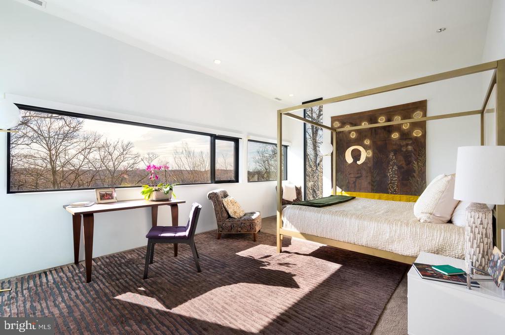 Bedroom with a gold four-poster bed and long windows overlooking trees.