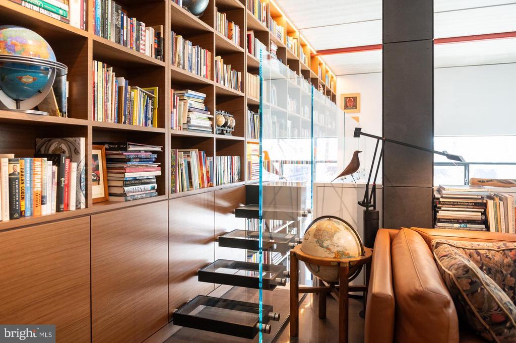 Home library with floor-to-ceiling bookshelves, a glass-sided staircase, and a leather sofa.