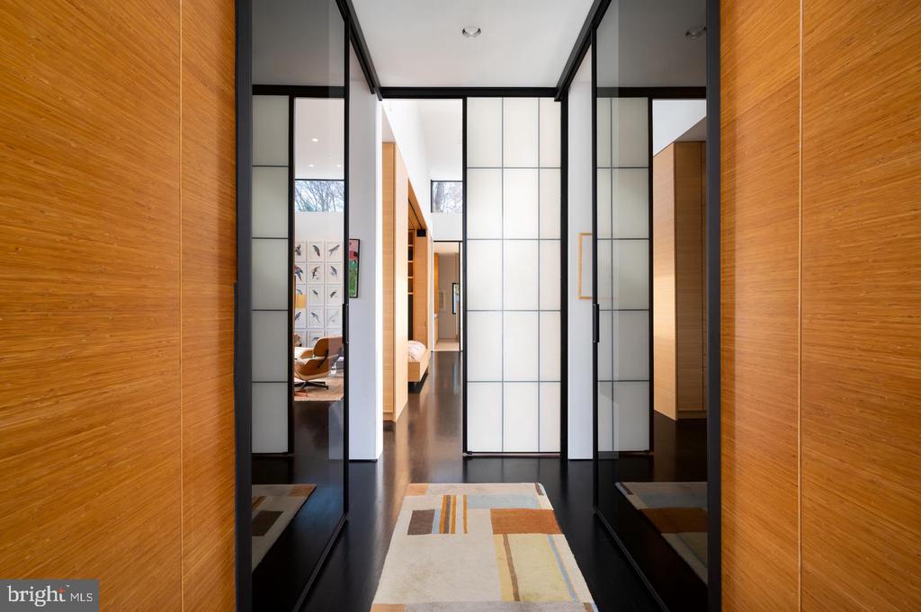 Modern hallway with wood-paneled walls, black-framed glass partitions, and a geometric runner rug.