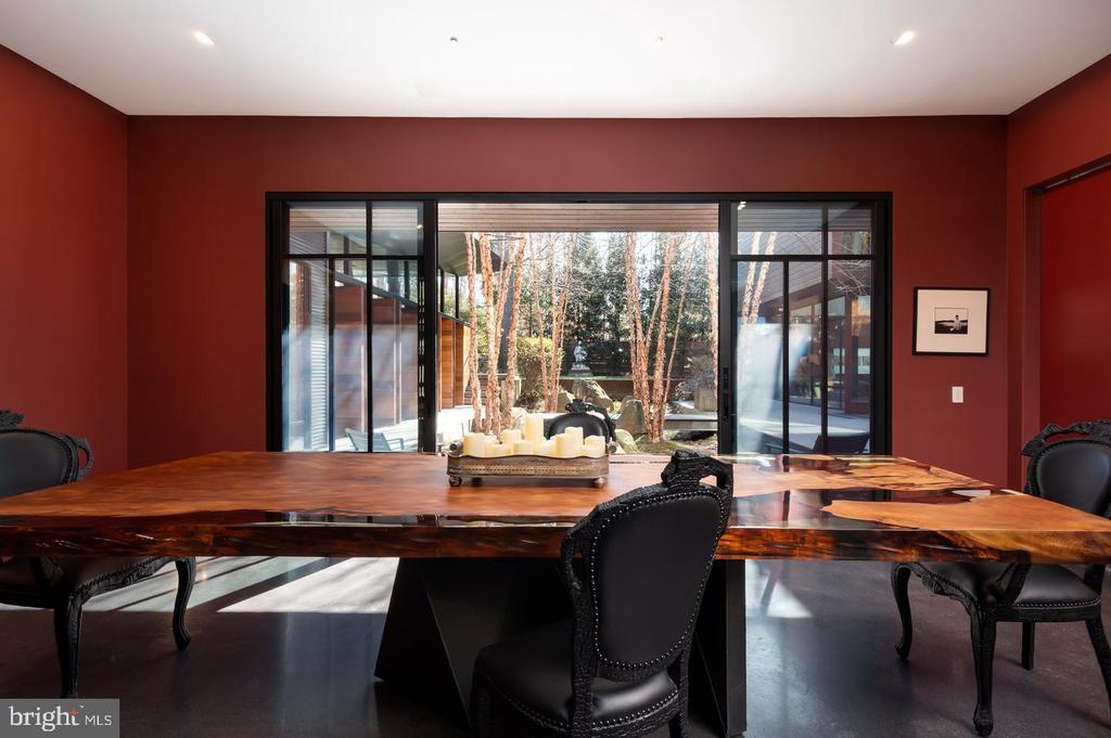 Dining room with a sculptural wood table and wide glass doors overlooking a wooded courtyard.