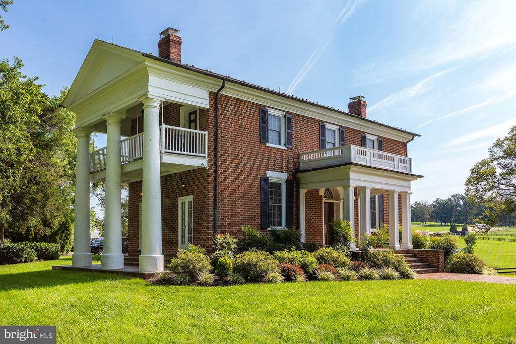 Two-story brick home with white columns, balconies, black shutters, and a landscaped lawn.