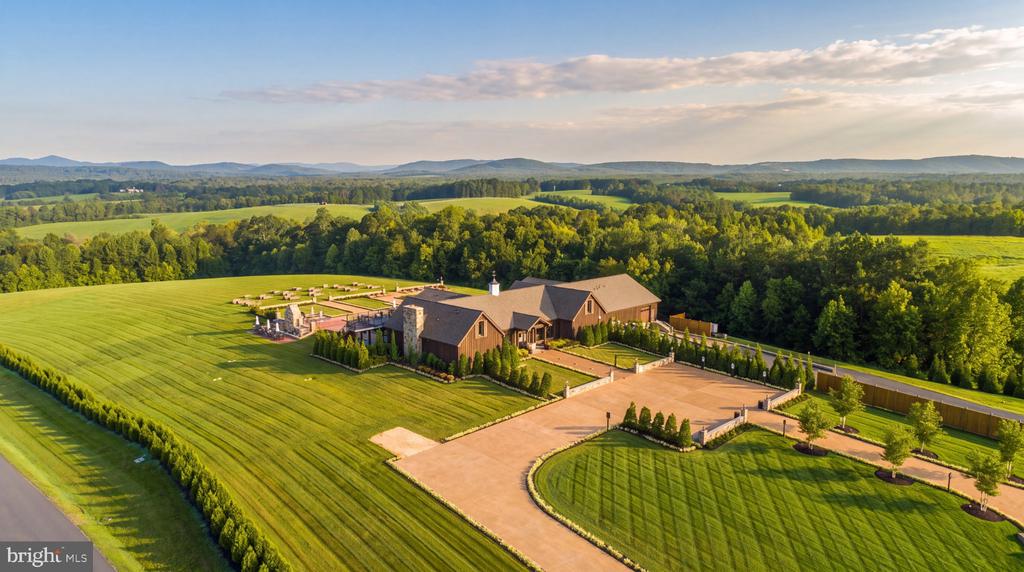 Country estate with a large house, manicured lawns, circular driveway, and wooded hills beyond.