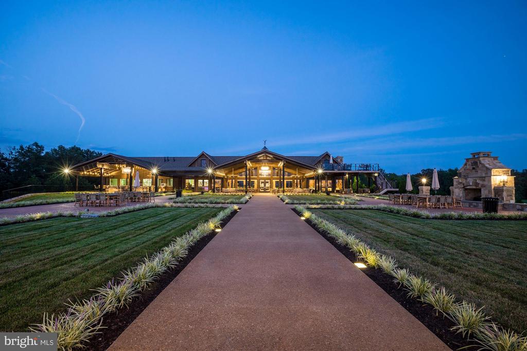 Large lit building at dusk, approached by a landscaped walkway with outdoor seating and a stone fireplace.