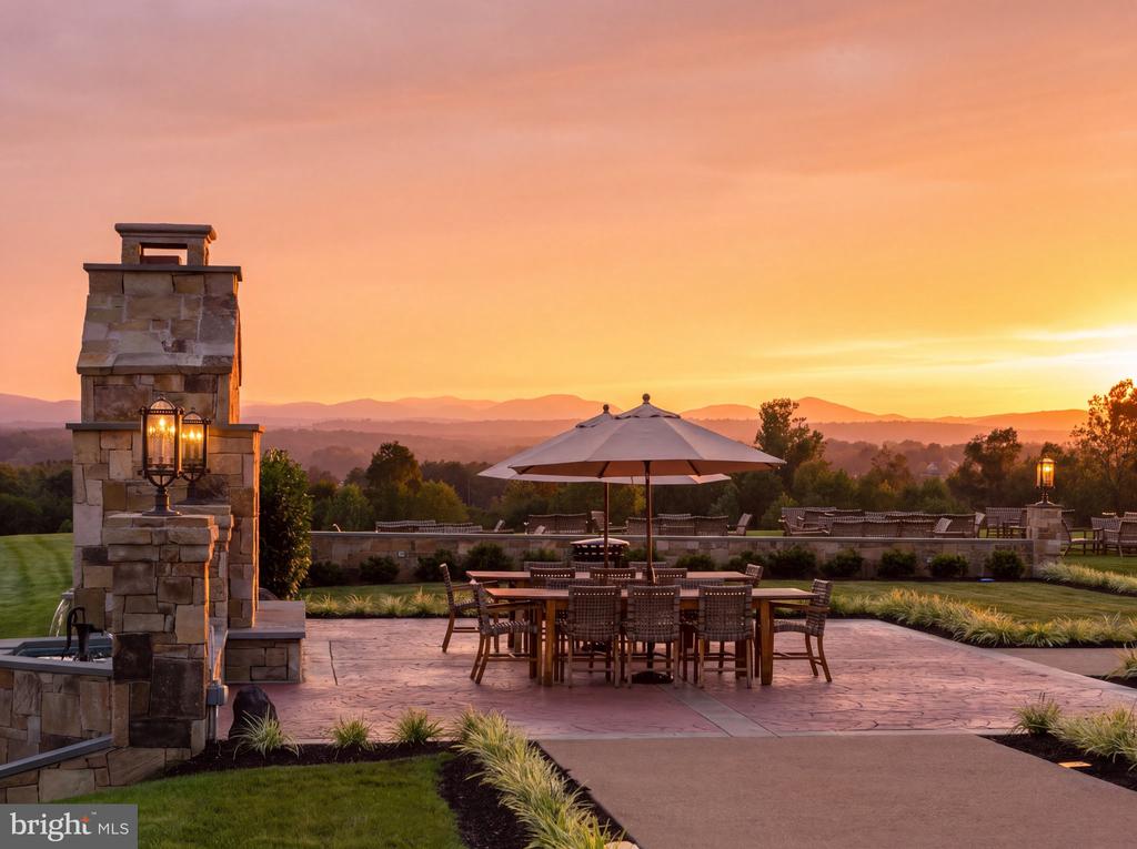 Outdoor patio with a stone fireplace, umbrella-covered dining set, and mountain views at sunset.