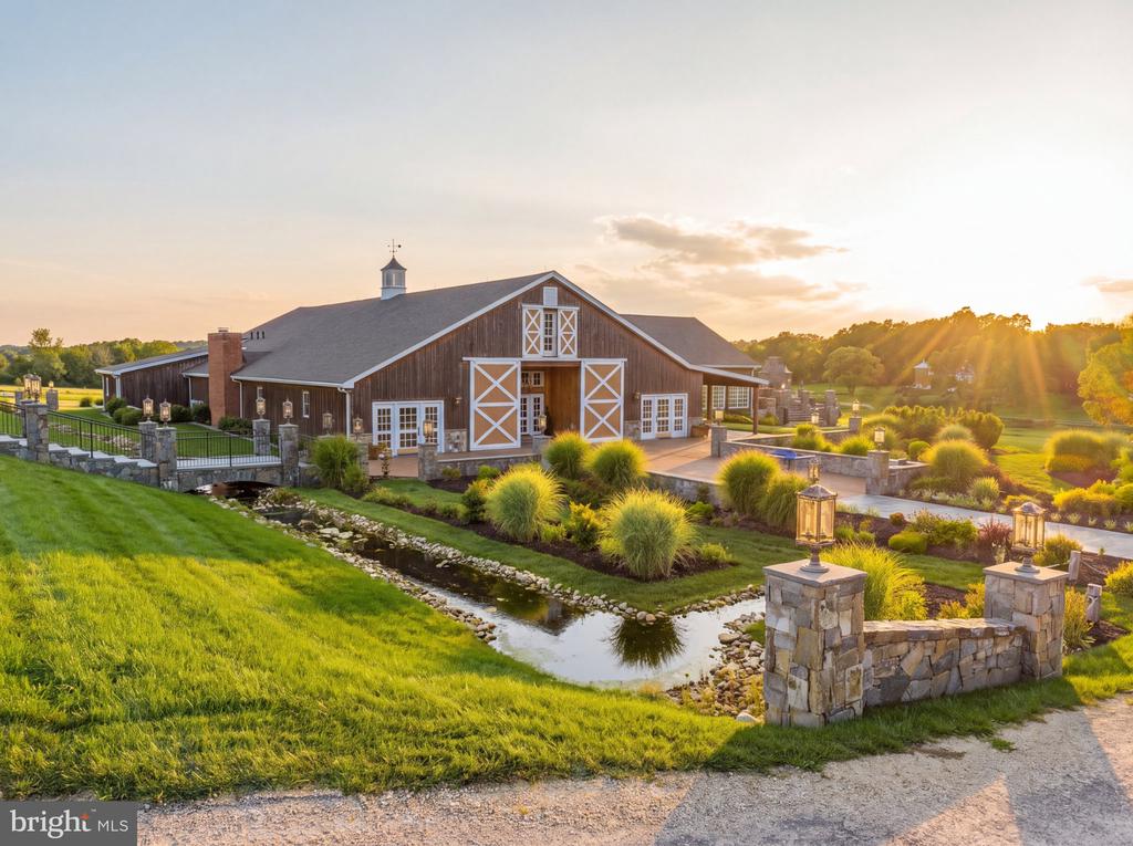 Barn-style property with white crossbuck doors, stone landscaping, and a stream at sunset.